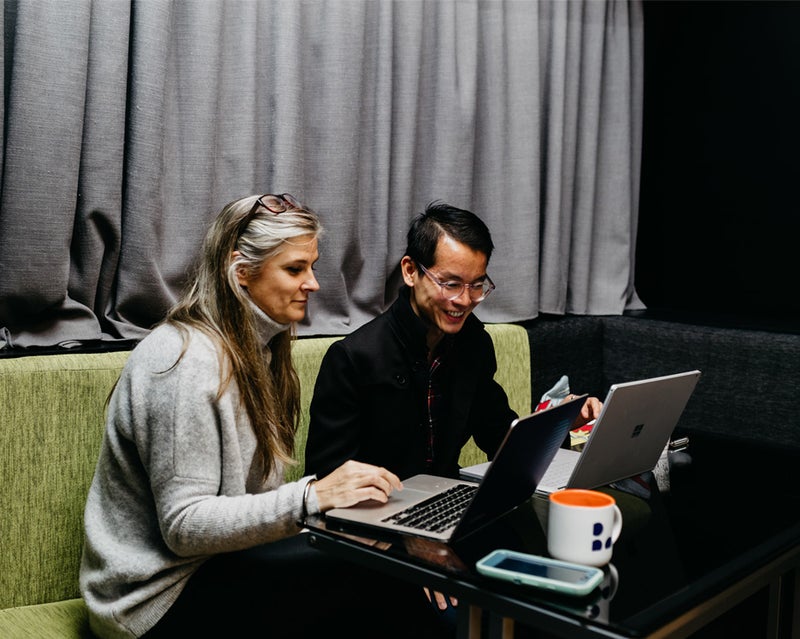 Two people sitting beside each other working at laptops