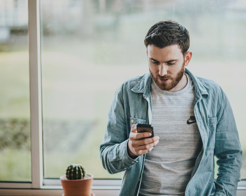 Man leaning against a window sill looking at his phone
