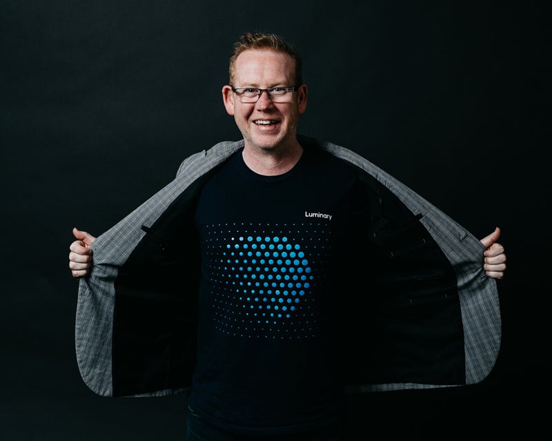 Man holding open jacket to show Luminary branded t-shirt